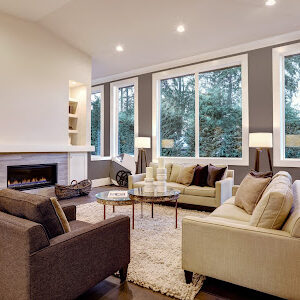 Chic living room design with dark floors. Furnished with glass top accent tables and beige sofas topped with brown pillows facing modern fireplace with built-in shelves in the wall. Northwest, USA